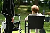 Zwei Senioren sprechen im Garten eines Pflegeheims, neben ihnen steht ein Rollator.