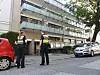 Zwei Polizisten vor einem Wohnhaus mit geparkten Autos an der Straße.