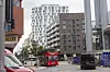 Roter Doppeldeckerbus fährt in einer Straße zwischen hohen Wohnhäusern und parkenden Fahrzeugen.