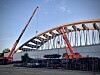 Zwei Kräne montieren eine geschwungene Brücke auf einer Baustelle.