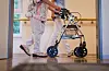 Zwei Personen gehen mit Rollator durch einen Flur.