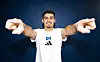 Martin Adeline im weißen HSV-Trikot vor blauem Hintergrund, Arme ausgestreckt und in die Kamera zeigend.