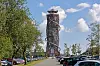 Harzturm am Torfhaus in Niedersachsen, umgeben von Bäumen und geparkten Autos unter blauem Himmel.