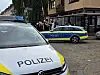 Polizeifahrzeuge sichern eine Straßenecke, Einsatzkräfte stehen im Hintergrund zusammen.