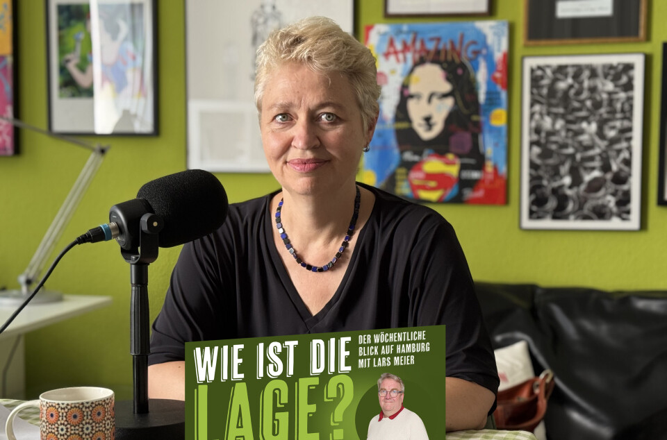 Frau an einem Tisch vor Mikrofon und buntem Hintergrund.