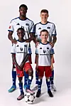 Vier Fußballspieler in weißen HSV-Trikots stehen im Studio, ein Ball liegt vorn am Boden.