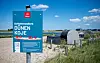 Blauer Hinweisschild vor einem Schlafstrandkorb in den Dünen an der Nordsee bei der Familienlagune Perlebucht.