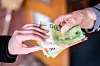 Junge Frau nimmt an einer Haustür mehrere Hundert Euro von einer älteren Dame entgegen.