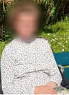Person sitzt auf einer Bank im Garten vor Blumen und Sträuchern.