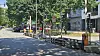Ruhige Straße mit Radweg, Absperrungen, parkenden Autos und Wohnhäusern unter Bäumen.