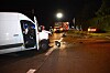 Weißer Lieferwagen mit offener Tür an nächtlicher Unfallstelle, Einsatzfahrzeuge und Trümmer auf der Straße.