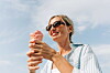 Frau mit Sonnenbrille isst draußen eine schmelzende rosa Eiskugel und lächelt.