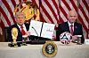 Trump zeigt die FIFA-Taskforce-Charta im Weißen Haus, Infantino sitzt daneben vor US-Flaggen und WM-Trophäen.