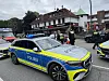 Polizei mit Einsatzfahrzeugen vor einem Restaurant; Einsatzkräfte und Passanten an einer regennassen Straße.