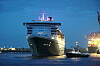 Großes Kreuzfahrtschiff bei Nacht im Hafen, beleuchtet neben hellen Hafenanlagen.