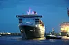 Großes Kreuzfahrtschiff bei Nacht im Hafen, beleuchtet neben hellen Hafenanlagen.