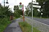 Gehweg neben Landstraße mit Haltestellenschild und Ortsschildern im Grünen.