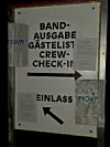 Aushang mit Band-Ausgabe, Gästeliste, Crew-Check-in und Einlass samt Pfeilen an einer Wand.