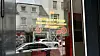 Schaufenster eines Technikgeschäfts mit gelber Werbung, Straßenspiegelung und vorbeifahrenden Autos.