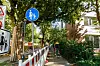 Schmaler Rad- und Fußweg an einer grünen Wohnstraße mit Verkehrsschildern und Häusern