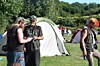 Menschen stehen vor Zelten auf einer Wiese und sprechen miteinander.