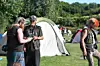 Menschen stehen vor Zelten auf einer Wiese und sprechen miteinander.
