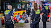 Polizisten sichern eine Haltestelle, mehrere Personen sitzen am Boden neben einem Bus.