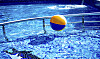 Bunter Wasserball schwimmt auf glitzerndem blauem Schwimmbecken im Sonnenlicht.