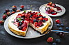New-York-Käsekuchen mit Erdbeeren, Blaubeeren und Kirschen auf dunklem Tisch