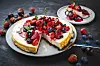 New-York-Käsekuchen mit Erdbeeren, Blaubeeren und Kirschen auf dunklem Tisch