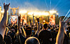 Festivalbesucher mit erhobenen Händen feiern vor den hell erleuchteten Wacken-Bühnen.