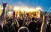Festivalbesucher mit erhobenen Händen feiern vor den hell erleuchteten Wacken-Bühnen.