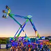 Leuchtendes Fahrgeschäft über einer Menschenmenge auf dem Jahrmarkt bei Dämmerung.