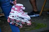 Person hält rosa Inlineskates mit weißen Rollen auf einem Gehweg.