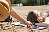 Frau liegt am Strand neben einem Smartphone, eine Hand greift danach.