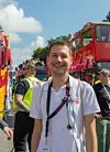 Lächelnder Mann steht zwischen roten Feuerwehrfahrzeugen auf der Straße.