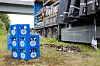 Gestapelte Wasserflaschen-Kisten neben einem beladenen Lastwagen unter einer Brücke.