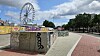 Riesenrad über graffitibedeckter Betonfläche am sonnigen Platz mit Wegen und Bäumen