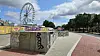 Riesenrad über graffitibedeckter Betonfläche am sonnigen Platz mit Wegen und Bäumen