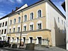 Historisches gelb-weißes Gebäude an einer Straßenecke mit mehreren Etagen und hohen Fenstern.