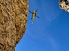 Gelber Hubschrauber zwischen steilen Felswänden vor blauem Himmel.