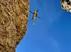 Gelber Hubschrauber zwischen steilen Felswänden vor blauem Himmel.