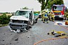 Einsatzkräfte arbeiten neben einem stark beschädigten Transporter und einem Feuerwehrfahrzeug auf einer Landstraße.