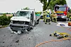 Einsatzkräfte arbeiten neben einem stark beschädigten Transporter und einem Feuerwehrfahrzeug auf einer Landstraße.