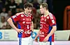 Zwei Handballspieler in roten Trikots stehen sich auf dem Feld gegenüber und sprechen.