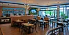 Modernes Café mit Holztischen, dunklen Stühlen, Bar und großen Fenstern zum Außenbereich.