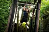 Person hängt an einem Kletterparcours im Wald zwischen Holzpfählen und Seilen.