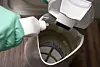 Hand mit Reinigungsmittel entkalkt einen geöffneten Wasserkocher.