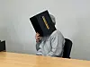 Person in grauem Hoodie sitzt am Tisch und verdeckt das Gesicht mit einer schwarzen Box.