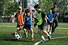 Mehrere Schulkinder spielen gemeinsam Fußball auf einem grünen Feld.